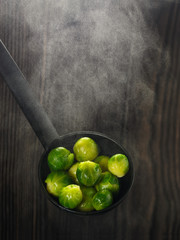 Boiled Brussels sprouts in the ladle on brown wooden background