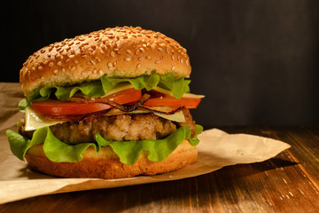 Cheeseburger with beef, lettuce, tomato, cheese, onion and bun with sesame on brown wooden table. Copy space.
