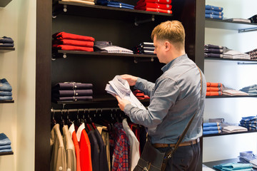 A man chooses outerwear in a store. adult Caucasian man looks among the rows of clothes on a hanger...