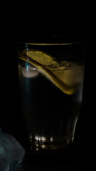 glass of water with lemon and ice on black background