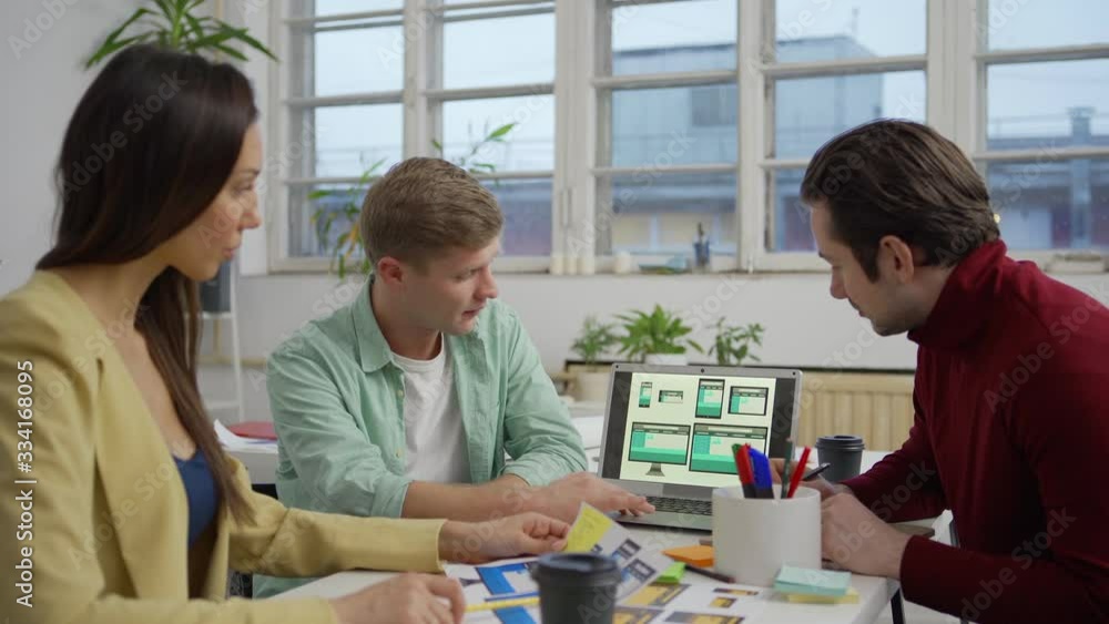 Wall mural tracking medium shot of team of three young marketing specialists and designers sitting at table in 