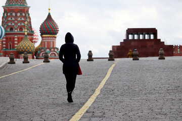 Quarantine in Moscow during COVID-19 coronavirus epidemic in Russia, empty streets in Moscow. Alone girl walking on Red square in Moscow on background of St. Basil's Cathedral and Lenin's Mausoleum