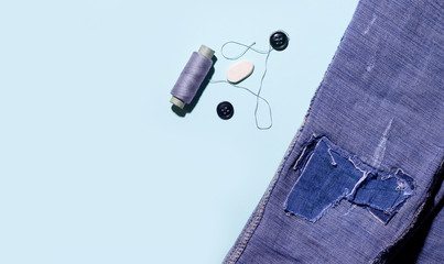 Threads and buttons on a blue background next to jeans. copy space.