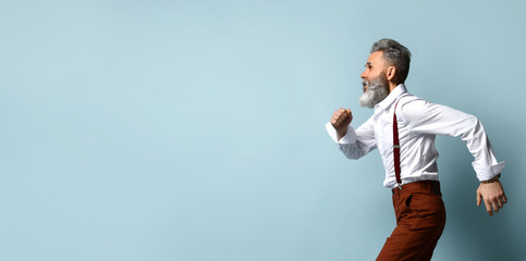 Gray-haired man in white shirt, brown pants and suspenders. He is running or posing standing...