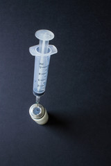 A syringe with a needle stuck in a medicine bottle on a black background with copy space. Concept:...