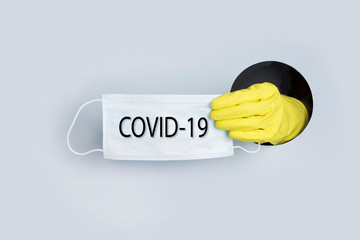 Coronavirus prevention Medical surgical masks in protective yellow gloves in hand through paper hole. COVID-19. Concept.