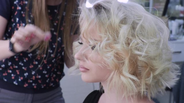 blonde woman with a haircut at a session with a hair stylist. Glamorous styling with curls, fixing the volume with hairspray