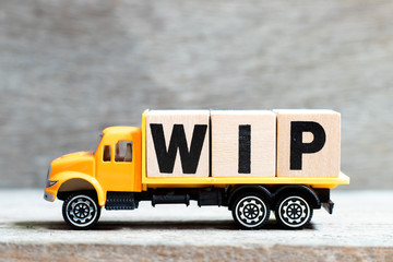 Truck hold letter block in word WIP (Abbreviation of work in progress) on wood background