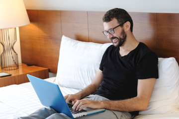 Young man is working from home during Coronavirus or Covid-19 quarantine. Man laying on bed using...
