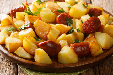 Tasty crispy fried potatoes with sausages and herbs close-up in a plate. horizontal
