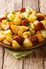 Fried potato wedges with sausages and herbs close-up in a plate. vertical