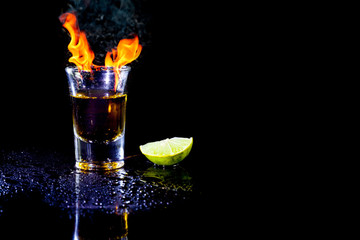 Cocktail blue burning in shot glass  with salt and lime, ice cubes on black background.