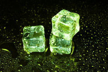 Green ice cubes on black table background.