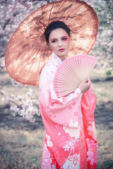 Beuatiful girl with japanese traditional kimono and umbrella in orchard during spring - 334173240