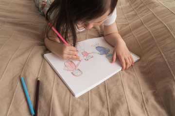 Cute girl draws a pencil drawing. A child learns to draw people. The child lies on the bed and...
