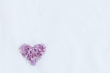 Fototapeta premium Lilac flowers mock up on white textile background. Little love heart on white texture background template. On the left down side 
