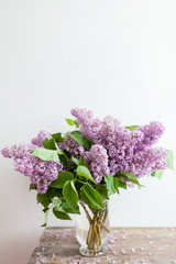Violet lilac flowers bouquet in glass vase on the wooden coffee table. Wildflowers bouquet mock up photo vertical orientation