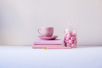 Feminine workspace, pink notebook, pink cup, pink candies on the white background. Back to school concept. Girls desk composition supplies. Pink, isolated, flat lay, copy space