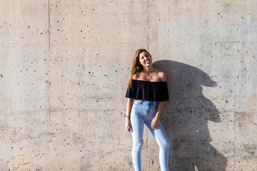Fototapeta na wymiar Beautiful girl leaning on grey wall, young friendly woman smiling and showing her tongue on a sunny day of summer
