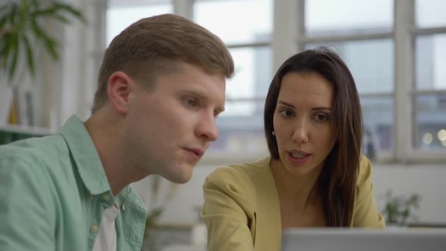 Zoom In Medium Shot Of Young Man And Woman Looking At Laptop Screen And Arguing While Discussing Project At Office