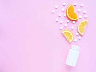 scattered vitamin pills from bottle with lemon and orange on pink background. Copyspace, flat lay. Concept boost immune system, medicine and tablets.