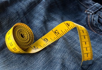 Measuring tape on blue jeans denim close up - jeans fashion mending or repair concept