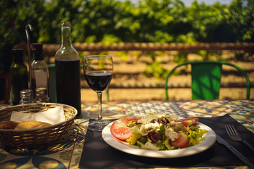 Mediterranean lunch in a farm restaurant, a glass, a bottle of wine and salad on a vineyard background