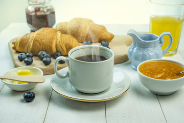 coffee with croissant, butter and blueberries stand on a white table