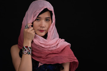 Portrait of beautiful Asian muslim woman wearing pink hijab looking at camera over black background.