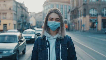 Young sad woman in medical mask raises head and looking to the camera road with cars and tram on background health and safety life COVID-19 coronavirus virus protection pandemic in world