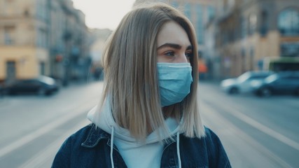 Fototapeta premium Close up view of a sad young caucasian woman wearing protective mask on the street road outdoor. Concept of health and safety life N1H1 covid19 coronavirus virus protection pandemic cars city