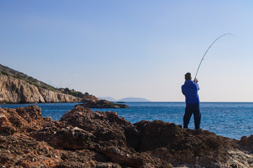 Unrecognizable fisherman a man stands on the sea shore with rocks and pulls the rod, biting the...