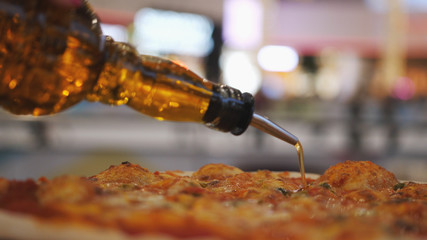 Close-up shot of pouring oil on pizza with blurred lights on background.