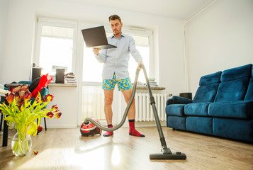 A man with a laptop and a vacuum cleaner in his apartment. Home Office