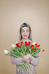 The lady with with closed eyes, holding bouquet of many tender red tulips.