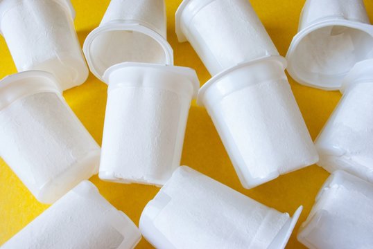Pile of white yogurt cups scattered on a yellow background. Ecological concept.