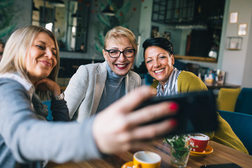 women talking in cafe while drinking coffee, using mobile phone