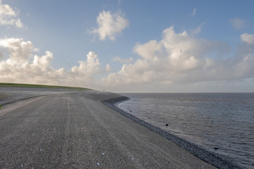 Wadden Sea dike with the silhouette of a walker on the horizon