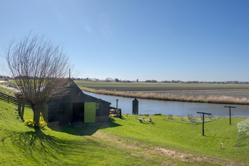 Fototapeta na wymiar Black old wooden shed with open green door at the bottom of a dike in a polder landscape