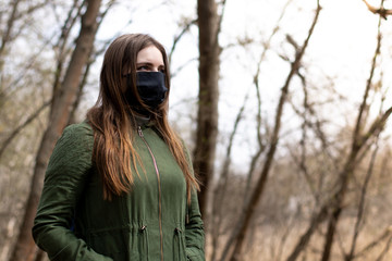 girl in a green jacket in a spring park in a medical black fabric mask close-up. example of the use of protection against infections.