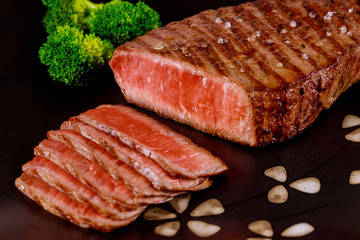 Juicy cooked beef sirloin with broccoli on black background.