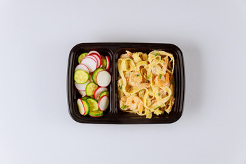 Black plastic container with pasta, shrips and fresh salad.