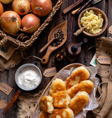 fried russian or ukrainian mini pies in oval wooden dish on rustic table with onion, pepper, flour