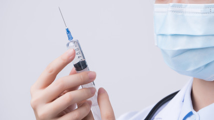 Doctor holding syringe with face mask, concept of young female physician injects coronavirus, COVID-19 vaccine on white background, close up, copy space