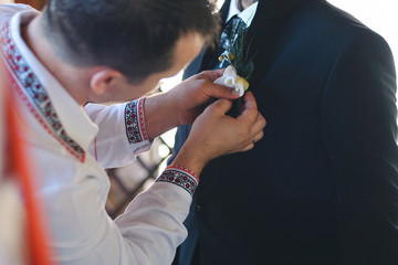 groomsman pinning boutonniere to groom's jacket