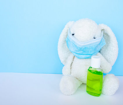 Easter quarantine coronavirus concept, white bunny rabbit with face protective mask and sanitizer on blue background. Copy space.