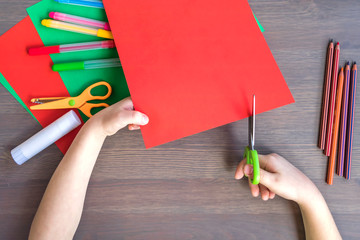 a child cuts red colored paper with scissors, a child makes a flower out of colored paper, a red...