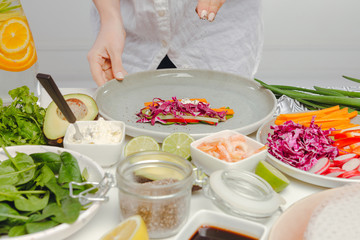 Obraz na płótnie Canvas Woman's hands adding seeds to spring roll with red cabbage, cheese, carrots, cucumbers. Table with spring rolls ingredients, organic and fresh vegetables.