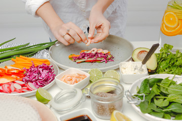 Obraz na płótnie Canvas Woman's hands adding shrimps to spring roll with red cabbage, cheese, carrots, cucumbers. Delicious spring rolls with seafood.