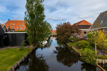 Fototapeta na wymiar Water canal between houses in Hindeloopen in Holland. There is a boat on the water and its reflection in the water.